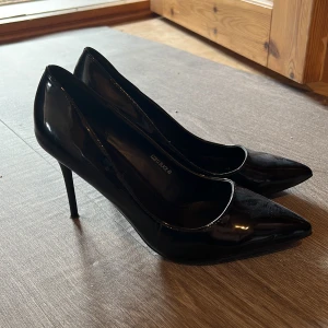 Svarta lackpumps från Jumex - Klassiska svarta pumps i glansigt lackmaterial från Jumex. Skorna har spetsig tå och smal hög klack som ger en elegant siluett. Perfekta för dig som vill ha en stilren och tidlös look med lite edge.