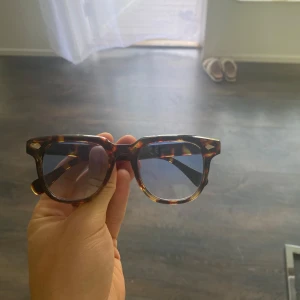 Bruna wayfarer-solglasögon i sköldpaddsmönster - Snygga wayfarer-inspirerade solglasögon med brun sköldpaddsmönstrad båge och blåtonade glas. Klassisk och tidlös design som passar till de flesta outfits. Bågarna är i plast och har coola detaljer vid gångjärnen.