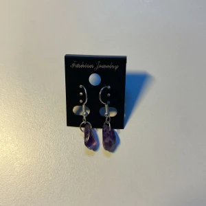 Handgjorda, Silvriga örhängen med lila stenar - Coola örhängen med silvriga krokar och oregelbundna lila stenar som hänger ner. Stenarna har en kristall-liknande känsla och ger ett unikt uttryck. Perfekta för dig som vill sticka ut med en färgklick och lite boho-vibe.