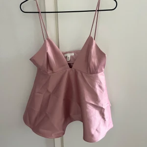 Rosa satinlinne med smala axelband - Supersött ljusrosa linne från H&M i glansigt satinmaterial. Toppen har smala axelband, v-ringning och en luftig, utsvängd passform som ger en riktigt trendig look. Perfekt att styla med jeans eller kjol för en chic vibe.