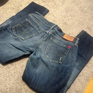 Blå jeans från Nolita, storlek 28 - Snygga blå jeans från Nolita med klassisk femficksmodell och coola slitningar framtill. Jeansen har raka ben, kontrastsömmar och en liten rosa detalj på bakfickan. Tillverkade i Italien och i mjukt jeanstyg. Midja - se bild, Innerbenslängd 70 cm. Storlek ca 28 28