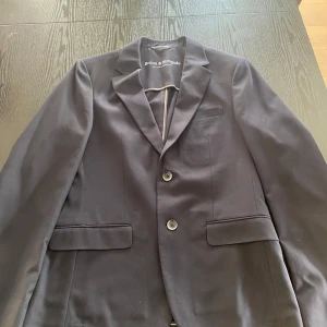 Kostym - Snygg slim fit mörkblå kostym från Bruun & Stengade med klassisk kavaj och matchande byxor. Kavajen har två knappar, smala slag och fickor med lock.
