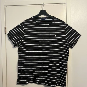 Svartvit randig t-shirt Polo Ralph Lauren - Svart t-shirt med vita horisontella ränder från Polo Ralph Lauren. Klassisk rund hals, korta ärmar och broderad logga på bröstet. Slim fit-modell i mjuk bomull som sitter snyggt och känns skön hela dagen.