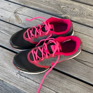 Nike träningssneakers svart/rosa - Snygga träningssneakers från Nike i svart och grått med starka rosa detaljer och snörning. Skorna har en sportig look med meshmaterial för bra andning och bekväm passform. Perfekta för gymmet eller löprundan.