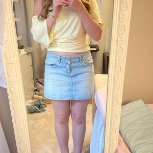 Ljusblå jeanskjol från Jsfn - Ljusblå jeanskjol från Jsfn med klassisk femficksdesign, bälteshällor och slitna detaljer framtill och baktill. Kjolen är kort och har en rak passform.