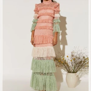 Pastellfärgad långklänning i spets - Superfin långklänning i pastellrosa, mintgrönt och vitt med volanger och spets. Klänningen har höga volangärmar, hög hals och flera lager med romantiska detaljer. Perfekt för dig som vill sticka ut med en unik och färgglad look.