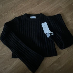 Svart ribbad stickad tröja Samsøe Samsøe - Svart stickad tröja från Samsøe Samsøe med breda ribbade ränder och rund hals. Tröjan har lång ärm och en något croppad passform, perfekt för lager på lager. Enkel och stilren design som funkar till många outfits.