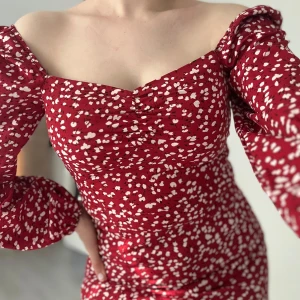 Röd blommig långärmad klänning - Supersöt röd klänning med vita blommor, puffiga långa ärmar och offshoulder-skärning. Figurnära passform med lätt rynk vid bysten och smickrande siluett. Perfekt för dig som vill sticka ut med en romantisk vibe.