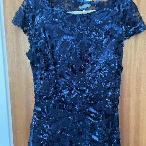 Mörkblå glittrig långklänning - Säljer en magisk mörkblå långklänning med glittriga paljetter över hela klänningen. Den har korta ärmar och en elegant, figurnära passform som ger en riktigt snygg siluett. Perfekt för bal eller fest där du vill sticka ut och glänsa.