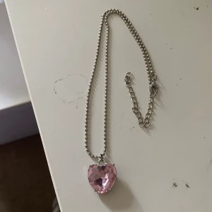 Halsband - Snyggt halsband med en silverfärgad kulkedja och ett stort, facetterat hjärthänge i rosa. Hänget är glittrigt och ger en riktigt söt och trendig look. Perfekt accessoar för att lyfta vilken outfit som helst.💕Jättestor sten!!😍Aldrig använd.Perfekt som present eller gåva❤️