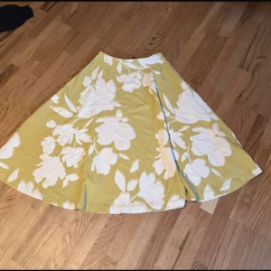 Gulblommig långkjol i bomull - Säljer en superfin långkjol i ljusgul färg med stora vita blommor. Kjolen har en härlig, svepande form och är perfekt för varma dagar. Materialet känns mjukt och luftigt, vilket gör den skön att bära. Perfekt för dig som vill sticka ut med en färgglad och somrig look!