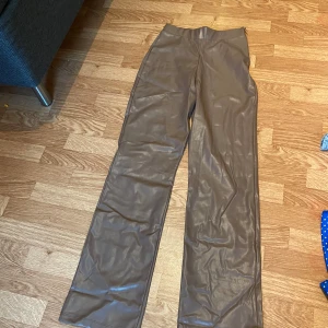 Bruna skinnbyxor från NLY Trend - Snygga bruna skinnbyxor från NLY Trend i storlek S. Byxorna har hög midja och raka, vida ben för en trendig look. Tillverkade i syntetmaterial med en mjuk insida. Perfekta för dig som vill sticka ut med en cool stil.