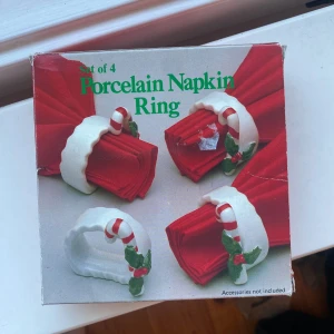 Servettringar  -  ett set med fyra porslinsservettringar med jultema. Perfekt för att ge din dukning en festlig touch till julmiddagen! Varje ring har en liten tomtefigur som håller en klocka. Snygg detalj för dig som gillar att fixa till det extra vid högtider.