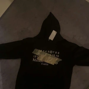 Maison Margiela svart hoodie med tryck - Svart hoodie från Maison Margiela med ikoniskt siffertryck och tejpdetalj på bröstet. Klassisk huva och långa ärmar, samt de typiska vita sömmarna i nacken. Perfekt för dig som gillar streetwear med lyxig touch. Spillans ny me tags pm för mer bilder och info