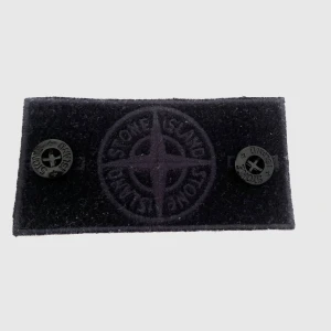 Svart Stone Island patch med knappar - Säljer en navy blue patch från Stone Island med klassisk kompasslogga i svart ton-i-ton. Två svarta knappar med Stone Island-tryck ingår. Perfekt att fästa på jacka eller tröja för en clean och stilren look. Obs! Ser lite dammig ut då den legat i en låda. Hör av er vid ev frågor :) 