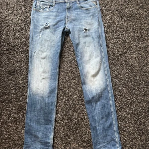 Replay Anbass ljusblå jeans slim fit - Säljer ett par Replay Anbass jeans i ljusblå tvätt med slitningar och hål på låren. Modellen är slim fit med klassisk femficksdesign och normal midja. Jeansen är i mjukt bomullsmaterial och har snygga detaljer vid fickorna.