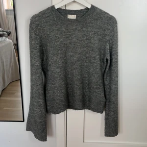 Grå stickad tröja med vida ärmar - Mysig grå stickad tröja med rund halsringning och lite vidare i ärmarna. Tröjan har ribbade muddar vid ärmslut och nederkant, perfekt för lager-på-lager under kyliga dagar. Enkel och stilren design som funkar till allt.
