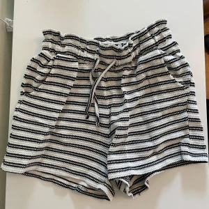 Randiga shorts med snörning - Snygga shorts med svartvita ränder och bekväm snörning i midjan. De har en loose passform och är perfekta för varma sommardagar. Materialet känns mjukt och luftigt, och midjan är elastisk för extra komfort. Shortsen har fickor på sidorna och en avslappnad vibe.