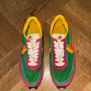 Nike x Sacai LDWaffle ”Pine Green”  - Nike x Sacai LDWaffle ”Pine Green” sneakers med grön mesh, rosa och gul mocka, dubbla orange swooshes och vit snörning. Skorna har svart mönstrad sula och dubbla detaljer på plösen. En riktigt unik och färgstark modell för dig som vill sticka ut. Väldigt bra skick och otroliga skor att ha i varmt väder. Storlek eu 41, us 8, uk 7. Priset är aningen förhandlingsbart