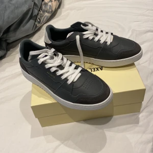 Axel Arigato dice lo - Snygga sneakers från Axel Arigato i svart och vitt med vita snören och detaljerad logga på sidan och sulan. Skorna har en klassisk låg siluett, rund tå och är tillverkade i skinn med kontrasterande vit häl. Perfekta för en clean och modern look. Helt nya 