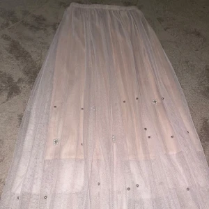 Ljusbeige tyllkjol med pärldetaljer - Superfin tyllkjol i ljusbeige mesh med pärlor och små silverfärgade detaljer. Kjolen har flera lager tunn tyll som ger ett drömmigt och luftigt intryck. Resår i midjan för skön passform. Perfekt för dig som gillar romantisk och trendig stil.