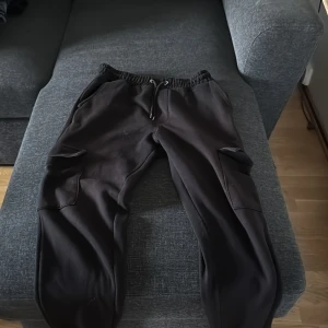 Svarta cargopants från Primark M - Svarta cargopants från Primark i mjuk bomullsmix. Byxorna har elastisk midja med snörning, stora cargofickor på sidorna och resår vid bensluten. Perfekta för en chill och avslappnad stil.