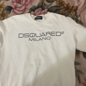 Vit sweatshirt från Dsquared2 - Snygg vit sweatshirt från Dsquared2 med svart tryck 'DSQUARED2 MILANO' på bröstet. Klassisk rund halsringning och långärmad modell. Tillverkad i mjuk bomull som är skön att ha på sig. Perfekt för en clean och stilren look. Såklart är den äkta också. Bara och höra av er vid pris eller annat