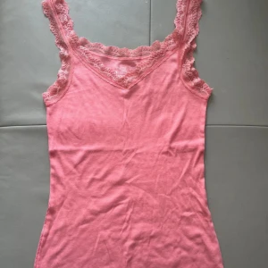 Rosa spetskantad linnetopp Esmara - Supersöt rosa linnetopp från Esmara med breda axelband och v-ringning. Toppen har fina spetsdetaljer längs ringningen och axelbanden. Tillverkad i mjuk bomull med lite stretch för extra komfort. Perfekt att styla med jeans eller kjol!