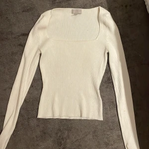 Vit ribbad långärmad topp H&M - Säljer en vit ribbad långärmad topp från H&M med fyrkantig ringning. Sitter tight och har en clean, stilren look som passar perfekt till jeans eller kjol. Materialet är mjukt och stretchigt för en bekväm passform.