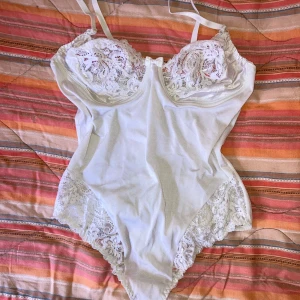 coquette vit body med spets - Supersöt vit body med spetsdetaljer över bysten och höfterna samt en liten rosett framtill. Materialet är glansigt och mjukt. Funkar som underklädesplagg alternativt topp! Väldigt bekväm och stretchig, passar mig perfekt som vanligtvis har S eller M😌 bh-storlek är typ 75B (?? Finns ingen lapp så  ungefär)