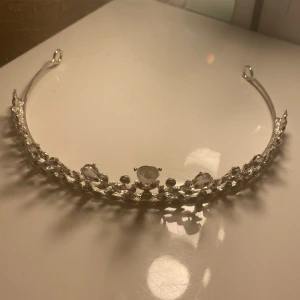 Glittrig silverfärgad tiara - Snygg tiara i silverfärg med glittrande stenar i olika former och storlekar. Perfekt accessoar för att känna sig som en riktig prinsessa. Tiaran har en elegant design med gnistrande detaljer som fångar ljuset. Saknar en diamant