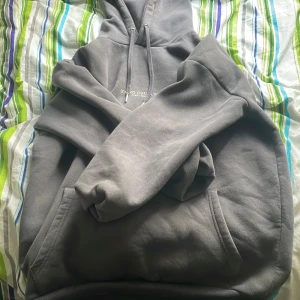 Grå hoodie från Icono Couture M - Snygg grå hoodie från Icono Couture med tryck både fram och bak. Tröjan har huva med snörning, känguruficka och relaxed fit. Perfekt för dig som gillar en clean och stilren look. Materialet är mjukt och skönt, troligtvis bomullsmix.