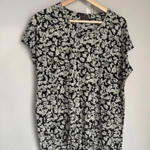 Blommig topp från Zeze Nordic - Svart topp från Zeze Nordic med vitt och ljusgrönt blommönster. Modellen har korta ärmar och rund halsringning. Toppens material känns mjukt och lätt, perfekt för dig som gillar en avslappnad men ändå snygg stil.