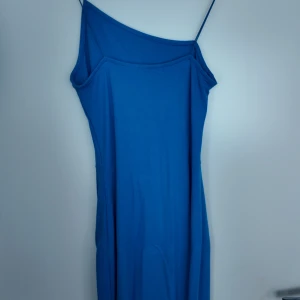 Blå oneshoulder långklänning - Snygg blå långklänning med oneshoulder och smala axelband. Klänningen har en enkel och stilren design, perfekt för dig som gillar minimalistiskt mode. Materialet känns mjukt och följsamt mot kroppen. Köpte klänningen från NAKD för ungefär 3-4 år sen och använt den endast 2 gånger. Materialet är flexibelt så passar storlekar från XS till M. Kommer ej ihåg exakta priset på den men tror den köptes för 500-600 kr. Pris kan diskuteras:)