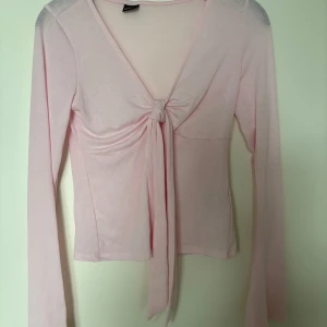 Ljusrosa långärmad topp Gina Tricot - Supersöt ljusrosa långärmad topp från Gina Tricot med v-ringning och knyt framtill. Tunn och mjuk i materialet, perfekt för lager-på-lager eller som den är. Snygg croppad passform och långa ärmar ger en trendig vibe.