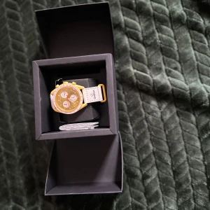 Omega gul och vit klocka - Säljer en Omega klocka med gul boett och detaljer, vit rem med Omega-logga och flera urtavlor. Klockan har en sportig och modern look med rund form och tydliga visare. Kommer i originalask och med kvitto.