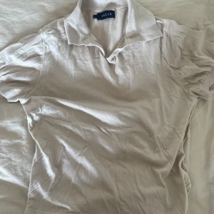 Piké krämvit Riley - En krämvit stickad kortärmad Piké från Riley i storlek s. 