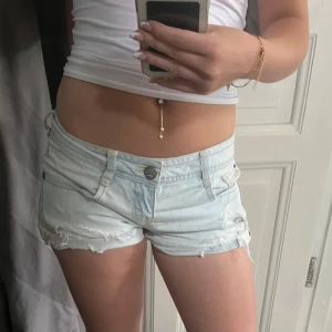 Ljusa jeansshorts från Bershka - Snygga ljusblå jeansshorts från Bershka med slitna detaljer och råa kanter. Klassisk femficksmodell med låg midja och knappgylf. Perfekta för sommardagar och ger en avslappnad vibe. Supersköna och lätta att matcha med crop tops eller linnen💗