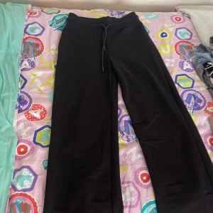 Svarta mjukisbyxor med snörning - Svarta mjukisbyxor med breda ben och snörning i midjan. Sköna och avslappnade, perfekta för chill dagar eller när du vill vara bekväm. Tillverkade i mjukt material och har en enkel, stilren look.