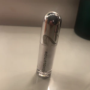 Revolution Glitter Muse flytande ögonskugga - Glittrig flytande läppglans från Revolution i nyansen Glitter Muse. Kommer i en snygg silvrig tub med metalliclock och ormsymbol. Perfekt för att skapa en skimrande look med mycket lyster.