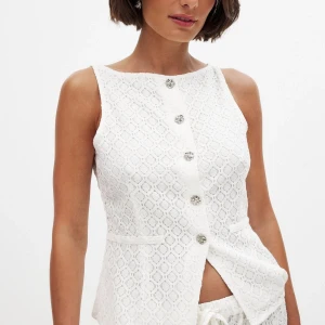 Vit spetsväst med silverknappar från NA-KD - Supersnygg vit väst i spets från NA-KD med silverfärgade knappar framtill. Västen har en figurnära passform och liten slits nertill. Perfekt att styla med matchande byxor eller jeans för en fräsch look. Nypris 499!