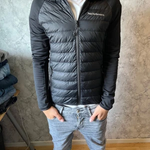 Svart pufferjacka Peak Performance S - Svart pufferjacka från Peak Performance i storlek S. Jackan har quiltad framsida och rygg, släta ärmar och dragkedja hela vägen. Snygg, sportig look med diskret logga på bröstet. Perfekt för kyliga dagar när du vill hålla stilen. Pris ej hugget i sten vid snabb affär. hör av dig vid minsta fundering!