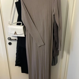 Mörk beige ribbad långklänning 157 - Långklänning i beige från 157, med ribbad struktur och lång ärm. Klänningen har en enkel, rak passform och rund halsringning. Perfekt för dig som gillar stilrena och minimalistiska plagg.