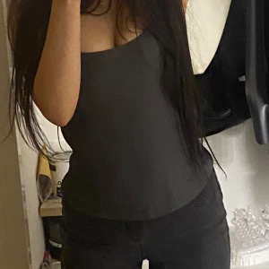 Mörkgrå croptop  - Säljer en mörk grå, stilren crop-top med asymmetrisk halsringning. Toppen är figurnära och har en enkel, clean look utan synliga detaljer. Perfekt att styla med jeans eller kjol för en snygg och modern vibe. (Passar inte tjejer med stora byst, därför ska jag sälja)