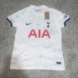 Tottenham Hotspur vit matchtröja Nike S - Snygg Tottenham Hotspur fotbollströja från Nike i vitt med diskreta ljusblå grafiska detaljer. Kortärmad modell med klubbmärke och Nike-logga på bröstet samt röd AIA-sponsor. Helt ny och aldrig använd.