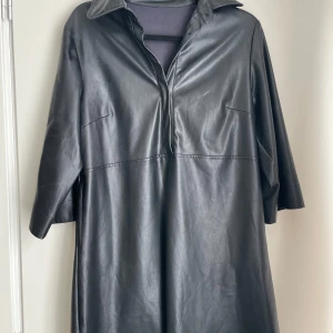 Svart klänning i skinnimitation – Strl S/M  - ✨ Svart klänning i skinnimitation – Strl S/M ✨  Stilren och trendig klänning i svart skinnimitation, perfekt för dig som vill ha ett plagg med både edge och elegans. Modellen har en avslappnad passform, krage och kort knäppning framtill – enkel att klä upp med klackar eller ner med sneakers för en mer avslappnad look.  ✔️ Oanvänd och i nyskick ✔️ Passar både vardag och fest ✔️ Bekväm, mjuk insida trots tuff look