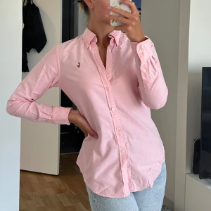 Rosa skjorta från Ralph Lauren - Snygg rosa skjorta från Ralph Lauren i skinny fit-modell. Skjortan har klassisk krage, långa ärmar och knäppning framtill. Broderad logga på bröstet och tillverkad i mjuk bomull. 