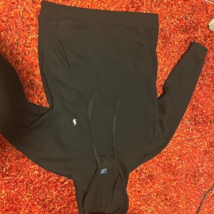 Svart hoodie från Polo Ralph Lauren - Svart hoodie från Polo Ralph Lauren med klassisk huva och snörning. Tröjan har en stor magficka och den ikoniska lilla broderade loggan på bröstet. Perfekt för en chill och stilren look. Tillverkad i mjuk bomull för extra komfort. Funkar som S också 