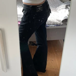 True Religion  - Svarta jeans från True Religion, modell Joey Low Rise Flare. Snygg låg midja och utsvängda ben med klassiska fickor bak med lock och knapp. 