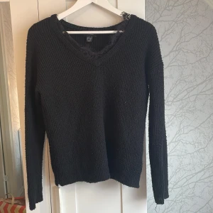 Svart stickad tröja med spets från Atmosphere - Svart stickad tröja från Atmosphere i storlek S. Tröjan har v-ringning med snygg spetsdetalj vid halsen och långa ärmar. Perfekt för dig som gillar en enkel men ändå lite extra look. Mjuk och skön att bära under kyligare dagar.